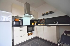 A compact kitchen with white cabinets, a microwave, an oven, and a black countertop. - Senlis - Éclat d'Époque (Senlis)