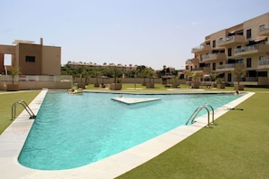 Une piscine rectangulaire à l’eau d’un bleu limpide, entourée d’une pelouse bien entretenue et d’un bâtiment de faible hauteur doté de balcons.