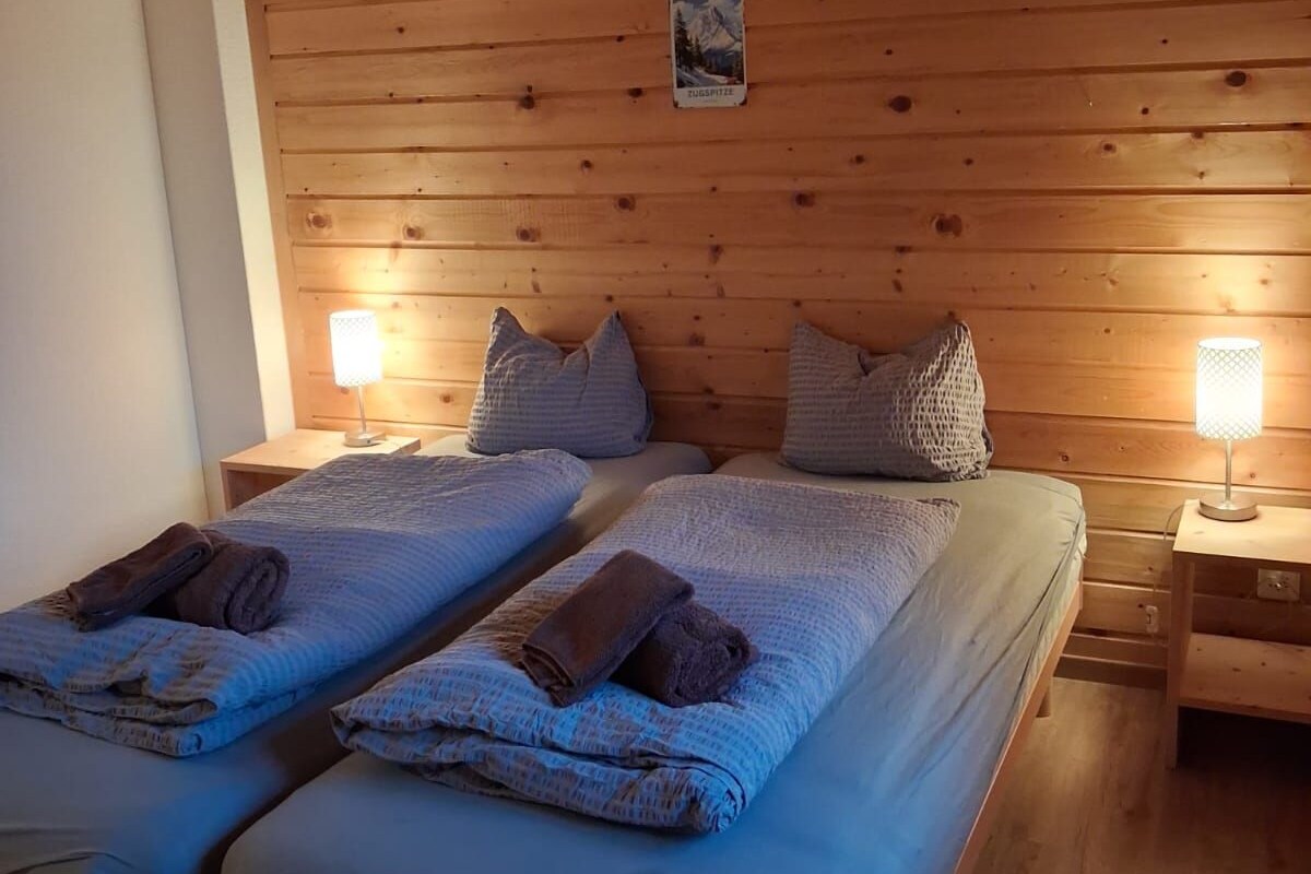 Huoneessa on parivuode, jonka molemmilla puolilla on yöpöytä, jossa on lamppu. Huoneen seinät ovat puupaneloidut.