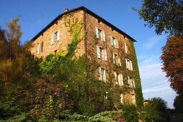 Un edificio de varios pisos de piedra con muros cubiertos de hiedra y múltiples ventanas.
