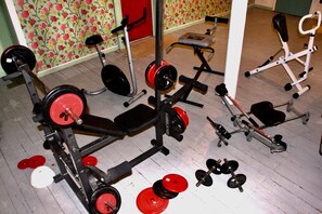 Un gimnasio en casa con equipo de ejercicio diverso, incluyendo una prensa de banca, mancuernas y una bicicleta estática.