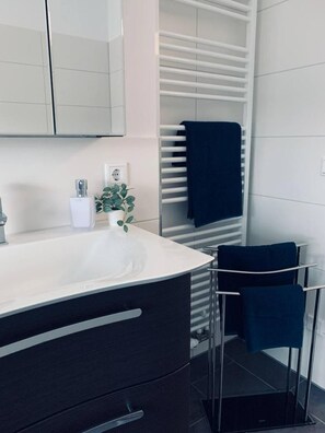 Un bagno moderno con lavandino bianco, mobili scuri, un porta asciugamani e una piccola pianta in vaso.