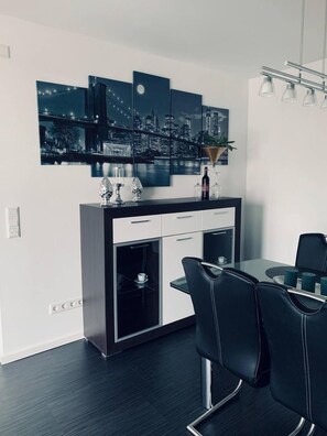Un'area pranzo moderna con schema di colori bianco e nero, un'opera d'arte con soggetto urbano sulla parete e un tavolo da pranzo con sedie.