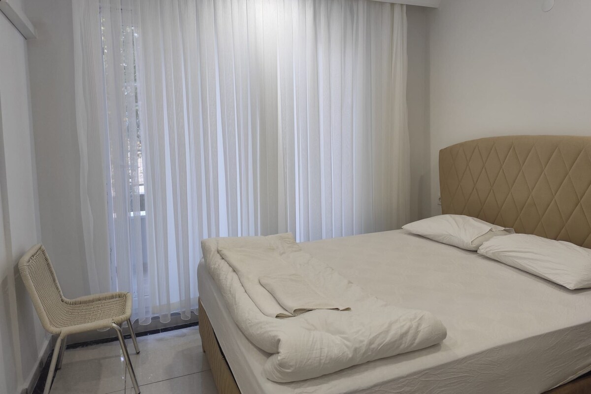A hotel room with a bed, a chair, and a window with curtains.