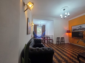Un salon comprenant un canapé, un hamac, un coin repas avec des chaises, un téléviseur et un sol à motifs.