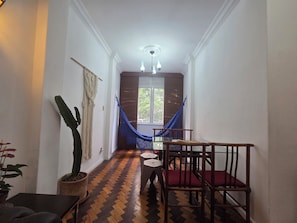 Un couloir qui donne sur un coin repas, avec une table et des chaises en bois, un hamac suspendu et une plante en pot.