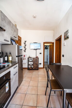 A modern kitchen with a dining area, a television mounted on the wall, and a hallway leading to another room. - Holiday Apartment 'La Casa Dei Bersaglieri' (Perugia)