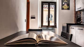 A room with a large open book on a table, a window with a view of a building, and a clock on the wall.