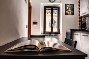 A room with a large open book on a table, a window with a view of a building, and a clock on the wall. - Holiday Apartment 'La Casa Dei Bersaglieri' (Perugia)