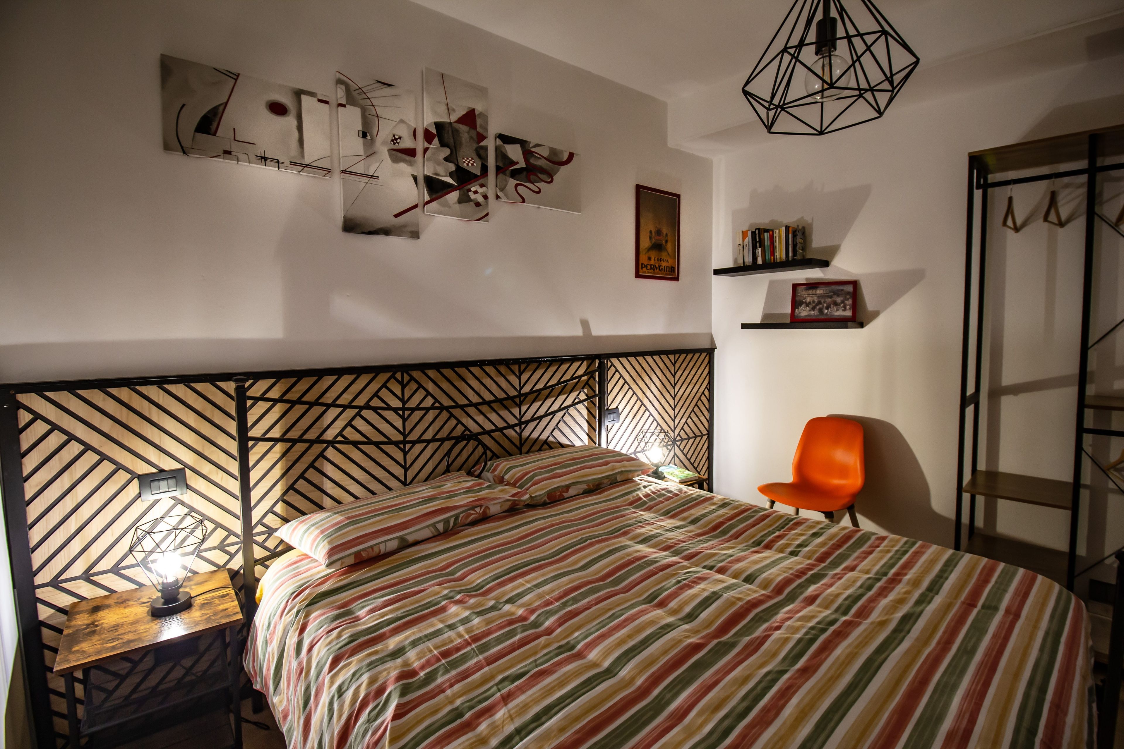 A bedroom with a bed, a chair, a nightstand, a geometric-patterned headboard, and wall art.