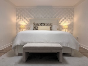 Un dormitorio con cama, almohadas, lámparas de noche y un banco.