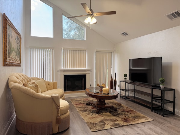Una sala de estar con sofá, chimenea, televisor y ventilador de techo.