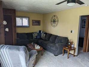 A living room with a sectional sofa, a coffee table, a small side table with a decorative item, and a ceiling fan. - Cozy 2-bedroom cabin in peaceful Linesville with AC (Linesville)