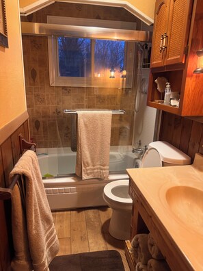 A bathroom with a bathtub, toilet, and sink, featuring wooden walls and a window with a view. - Cozy 2-bedroom cabin in peaceful Linesville with AC (Linesville)