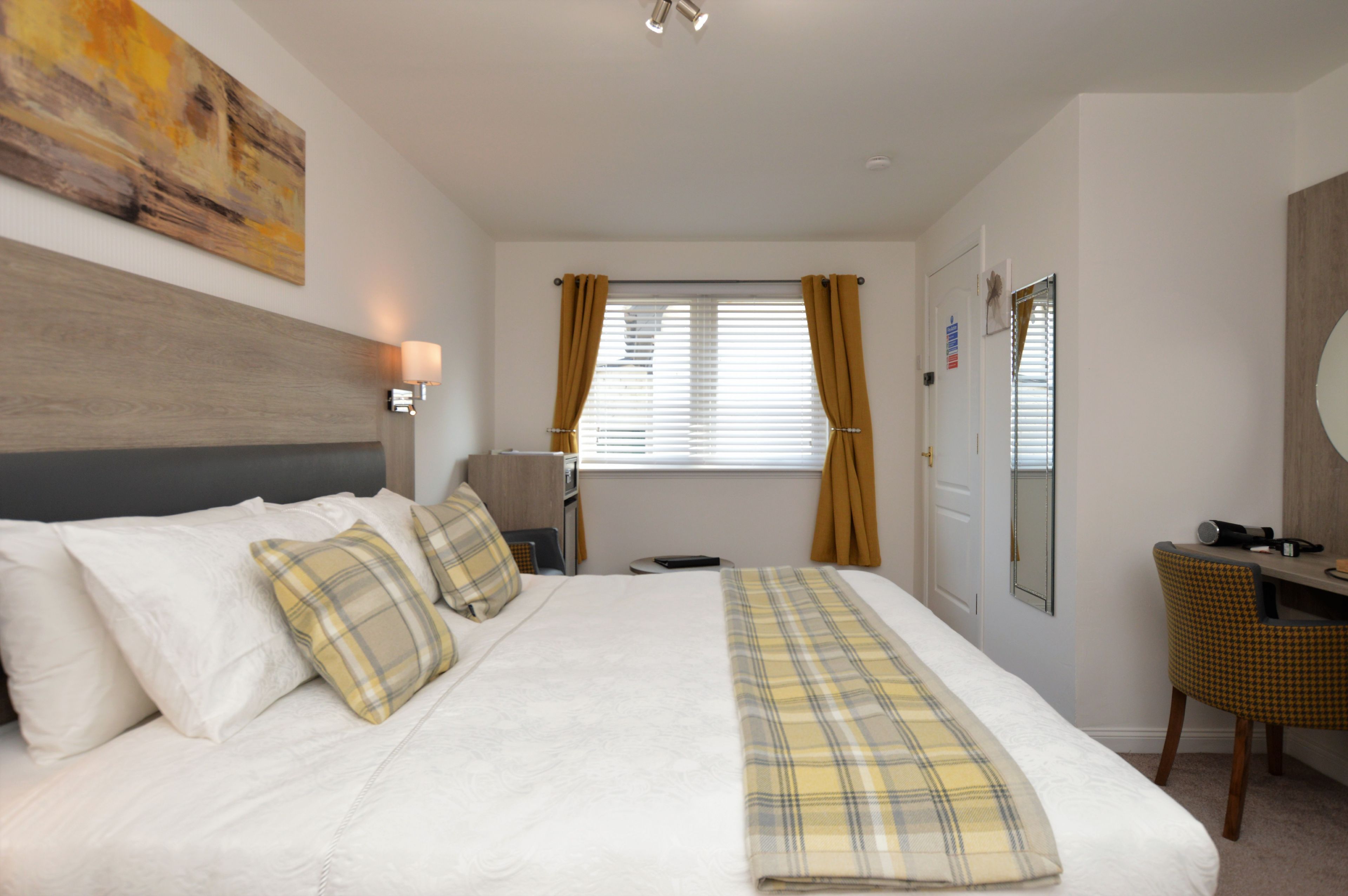 Een hotelkamer met een bed, een bureau, een stoel, een raam met gordijnen en een schilderij aan de muur.
