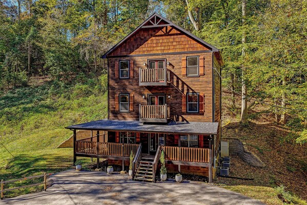 A two-story wooden cabin with a balcony, a porch, and a staircase leading to the entrance. - Spacious Retreat with Hot Tub, Firepit & Easy Access (Sevierville)