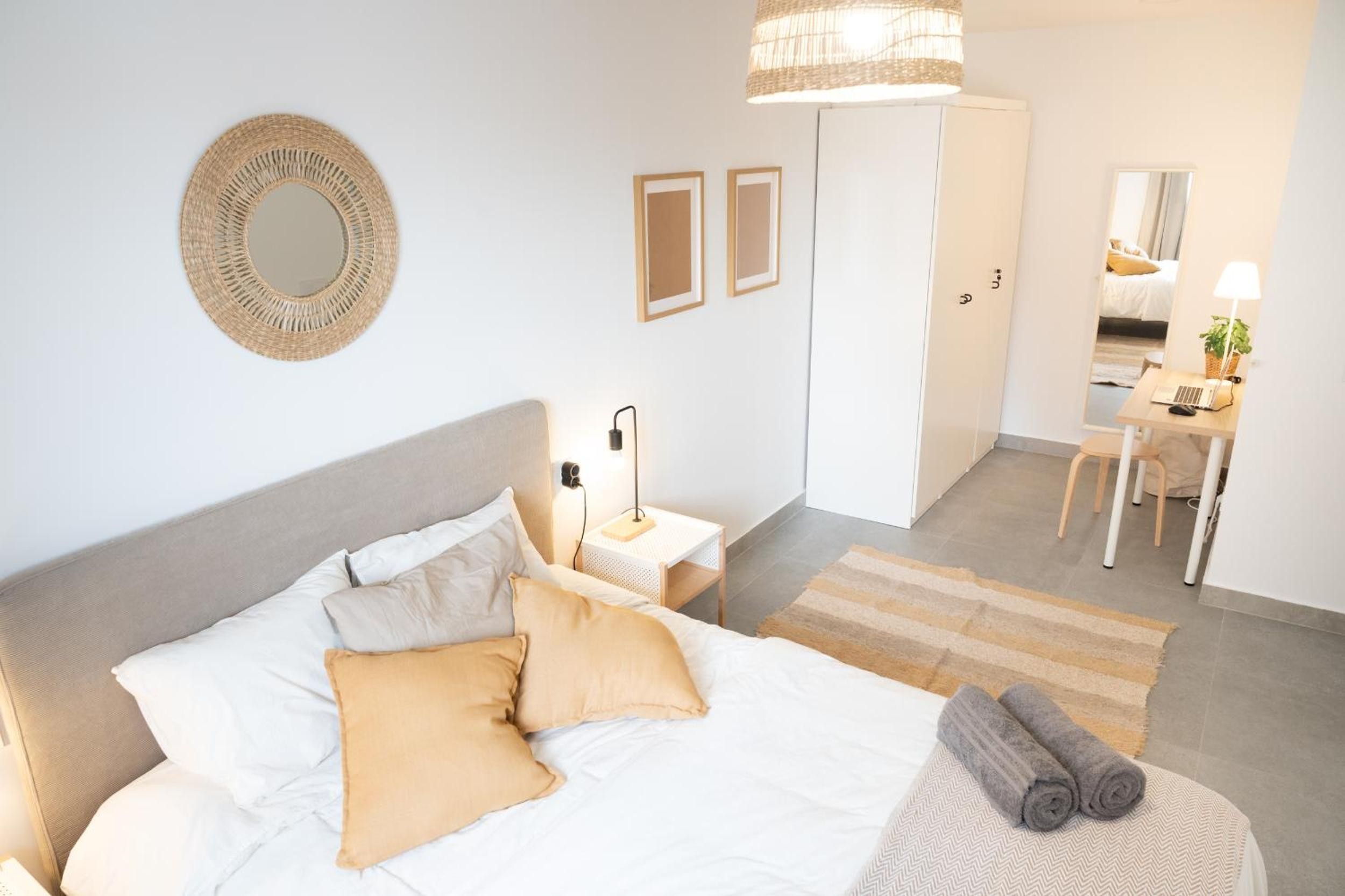 A hotel room with a bed, bedside table, lamp, and a view of the adjacent room.