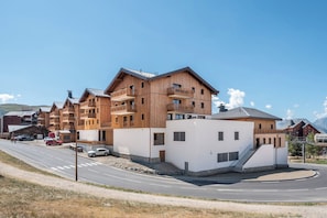 Un immeuble en bois à plusieurs étages, doté de balcons et d’une façade blanche, avec une route au premier plan.