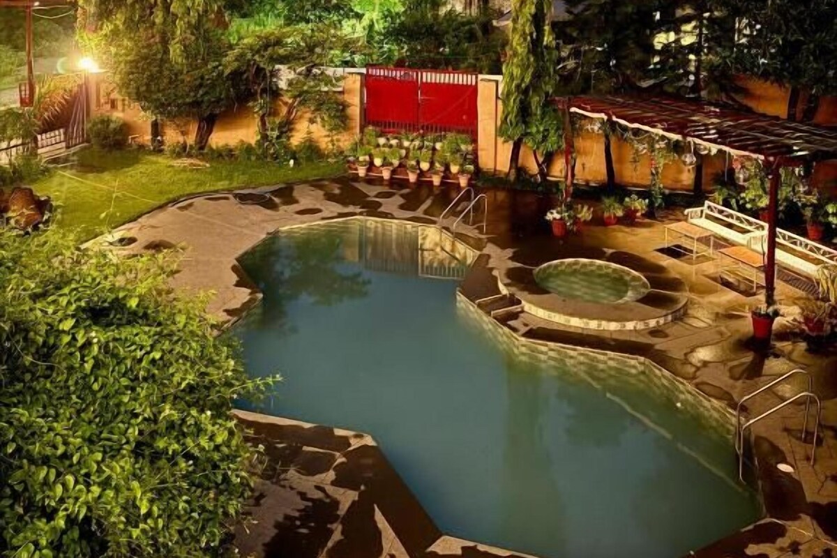 Ein Poolbereich mit kreisförmigem Design, umgeben von Grün und einem roten Gebäude im Hintergrund.