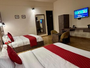 Ein Hotelzimmer mit zwei Betten, einem Schreibtisch, einem Sessel, einem Fernseher und einem Spiegel.