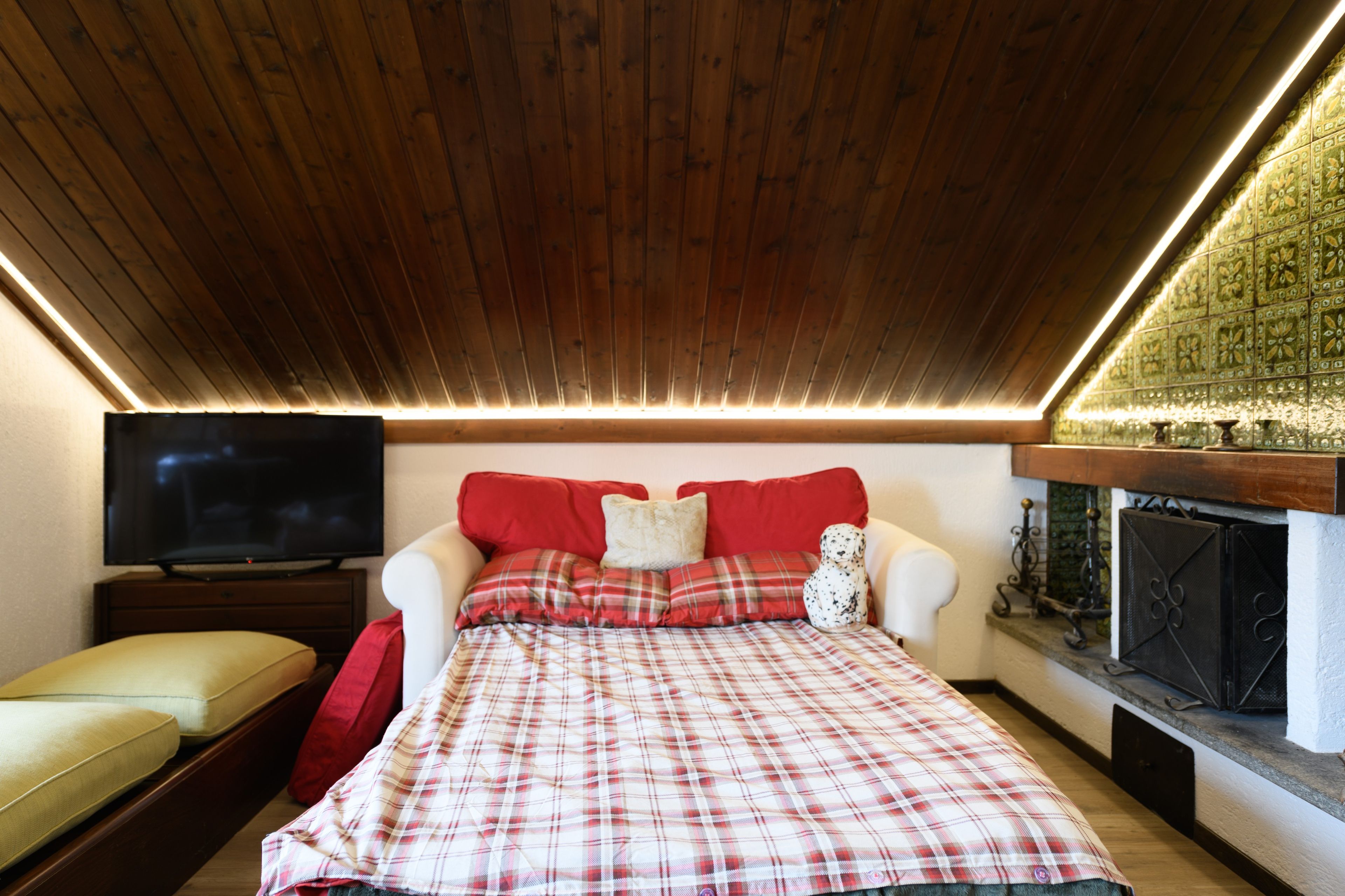 Ein Schlafzimmer mit Holzboden, einem Fernseher, einem Bett mit Karomuster-Bettwäsche, einem roten Sofa und einem Kamin.