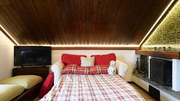Ein Schlafzimmer mit Holzboden, einem Fernseher, einem Bett mit Karomuster-Bettwäsche, einem roten Sofa und einem Kamin.