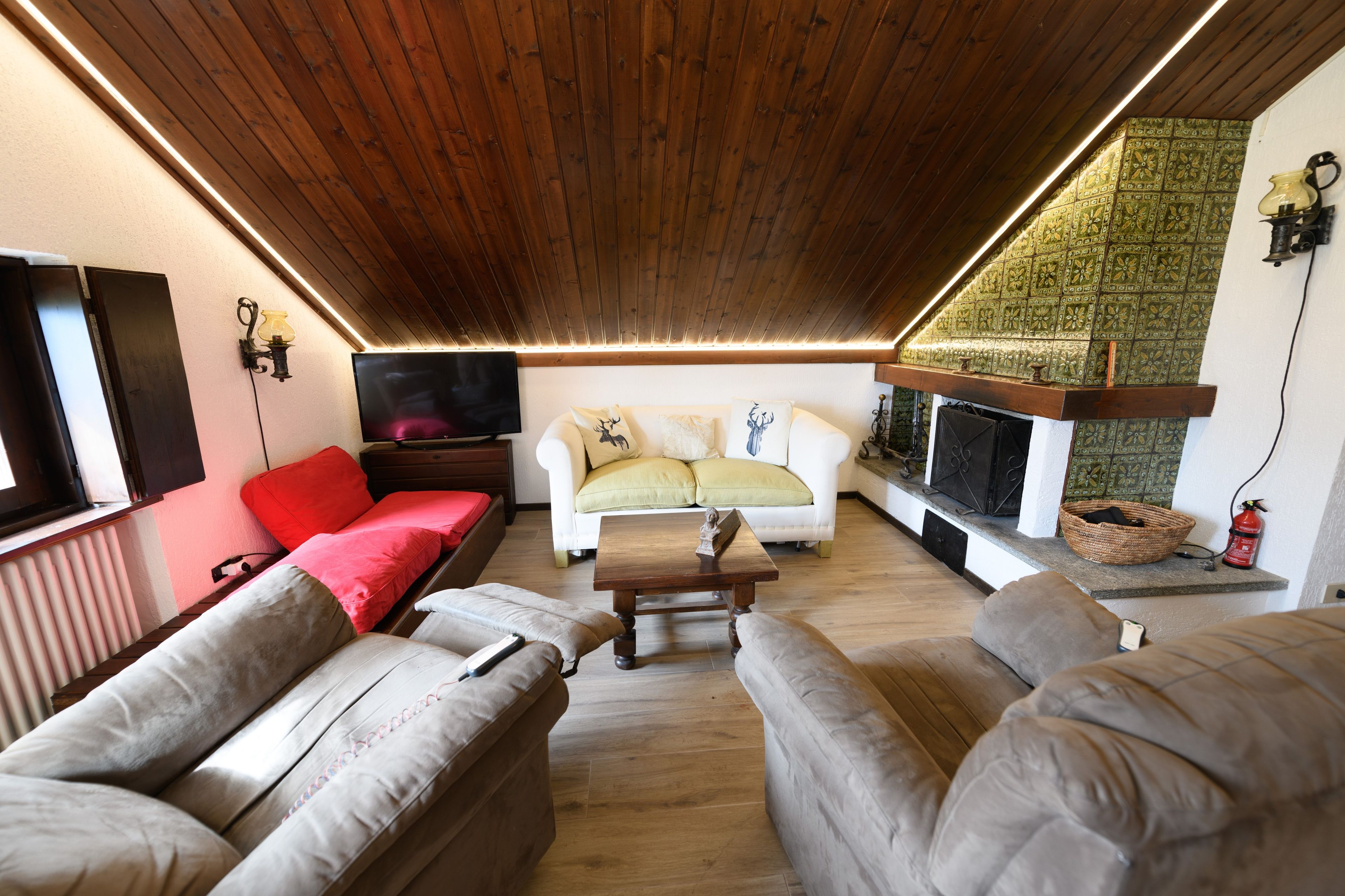 Ein gemütliches Wohnzimmer mit Holzbalkendecke, einem Flachbildfernseher, einem Kamin und einer Sofagarnitur.