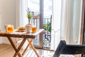 Un balcón con una mesa de madera, dos vasos de zumo de naranja, un muffin y un vaso de zumo de naranja.