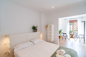Habitación de hotel con cama, mesita de noche, armario, balcón con mesa y sillas, y vistas al exterior.