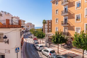 Vista de la calle con coches estacionados, un paso de peatones y edificios con balcones.