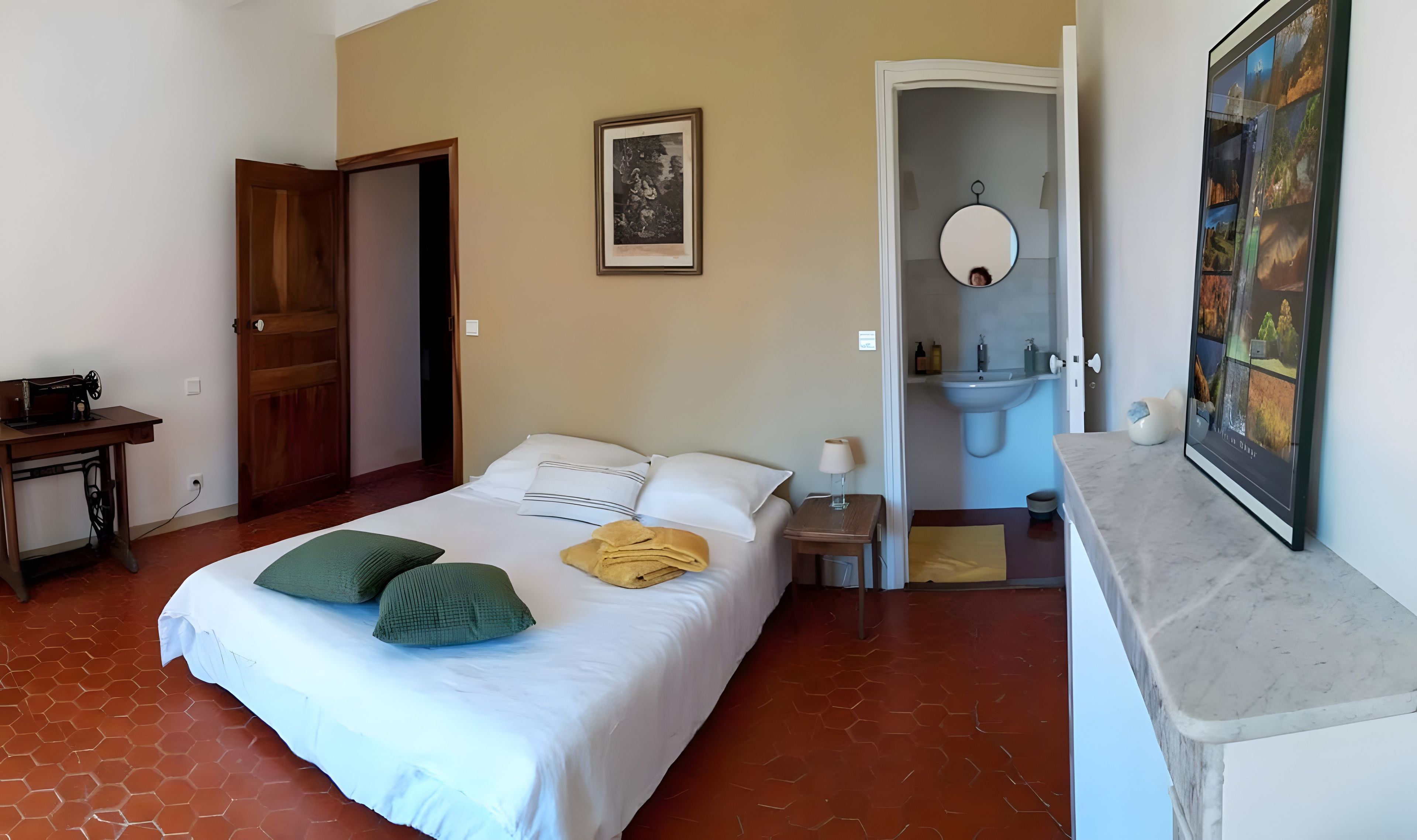 A hotel room with a bed, a desk, a bathroom, and a painting on the wall.