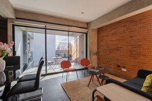 A modern living room with a sofa, a dining table, and chairs. There is a large sliding glass door leading to an outdoor area with a view of the city. - Apartment with Beautiful Views | 202 (Puebla)
