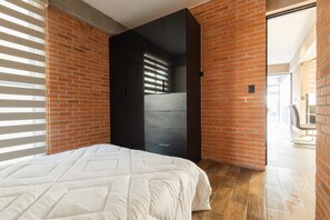 A modern bedroom with a brick wall, a large bed, and a dark wardrobe. - Apartment with Beautiful Views | 202 (Puebla)