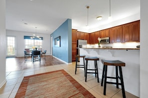 Una cocina moderna con armarios de madera, electrodomésticos de acero inoxidable y una zona de bar con taburetes.