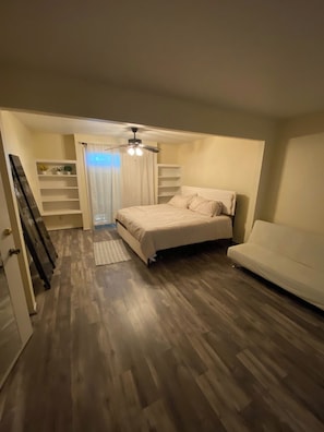 Une chambre à coucher avec un lit, un canapé blanc, un ventilateur de plafond et des étagères intégrées.