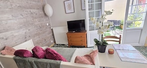 Une chambre avec un lit, une commode, un téléviseur et une fenêtre où est posée une plante orchidée.