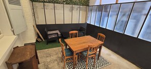 Une petite pièce avec une table et des chaises en bois, un canapé, une fenêtre à vitres dépolies et un tapis à motifs.