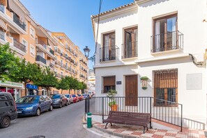 Vista de la calle con coches aparcados, un banco y edificios de varios pisos con balcones.