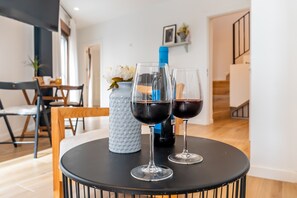 Una mesa de comedor con dos copas de vino y una botella, un florero con flores, y una escalera al fondo.