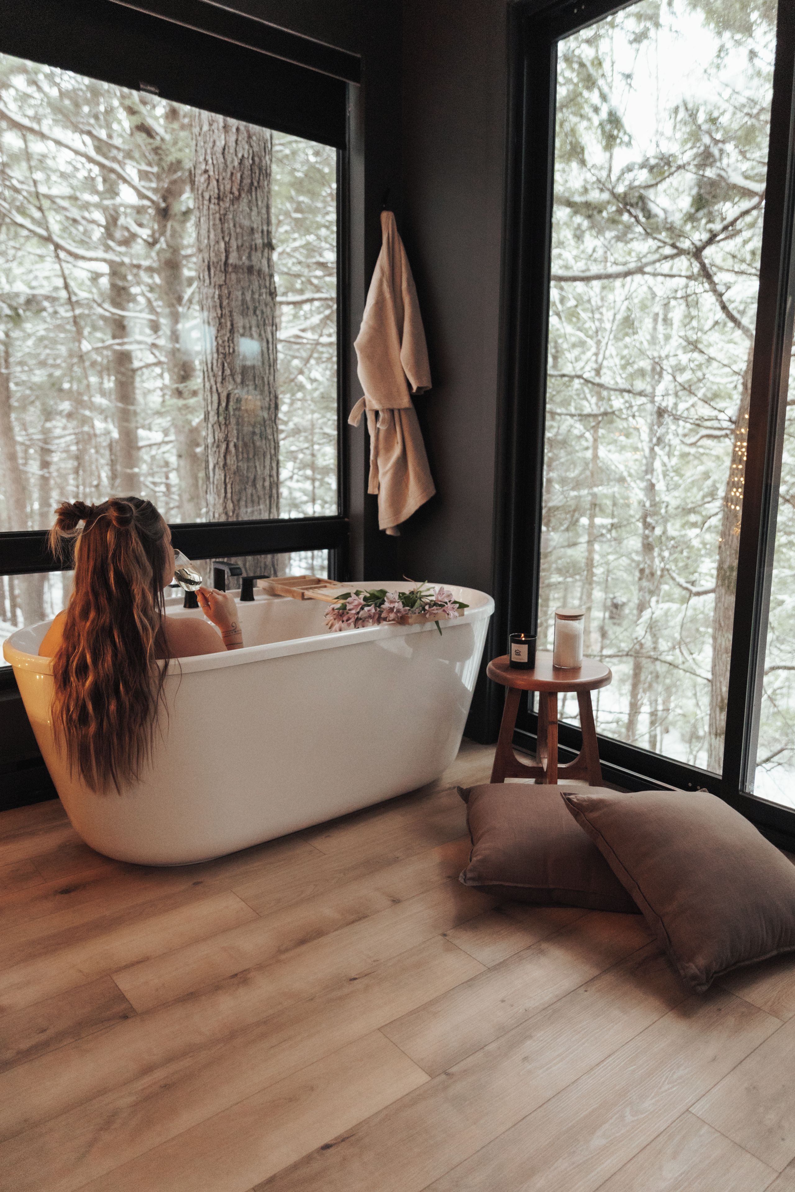 Une salle de bain avec une baignoire, un plancher en bois et une fenêtre donnant sur les arbres.