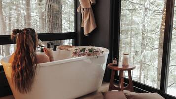Une salle de bain avec une baignoire, un plancher en bois et une fenêtre donnant sur les arbres.