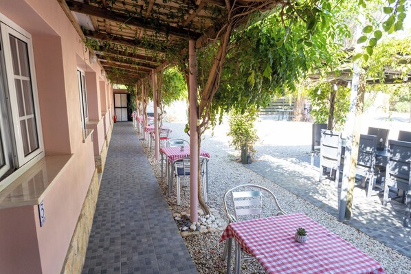 A covered outdoor seating area with tables and chairs, a tiled walkway, and a building with a pink facade. - Quinta Aida Farmhouse Rooms (Lagoa)