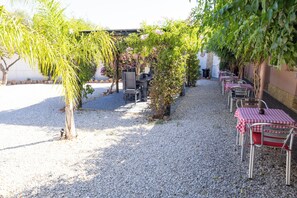 An outdoor seating area with tables and chairs, gravel ground, and greenery. - Quinta Aida Farmhouse Rooms (Lagoa)