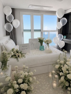Une chambre à coucher avec un lit, des fleurs blanches, des bougies et une pancarte sur laquelle on peut lire : « Voulez-vous m’épouser ? »