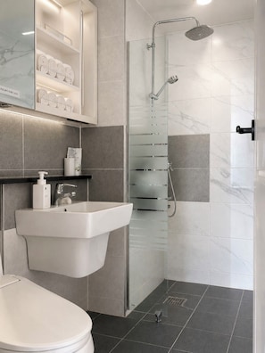 Une salle de bain moderne avec un lavabo blanc, des toilettes, une cabine de douche en verre et une zone de douche carrelée en marbre.