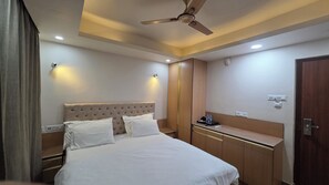 Une chambre d’hôtel comprenant un lit, une table de chevet, une armoire, un ventilateur de plafond et une lampe fixée au mur.