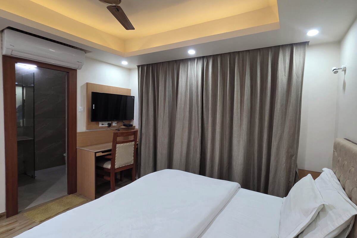 Une chambre d’hôtel comprenant un lit, un bureau avec un téléviseur à écran plat, un ventilateur de plafond et une grande fenêtre avec des rideaux.