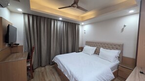 Une chambre d’hôtel équipée d’un lit, d’une télévision, d’un ventilateur de plafond et d’une fenêtre avec des rideaux.