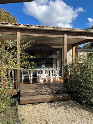 Een overdekt terras met een eettafel en stoelen, omgeven door begroeiing.