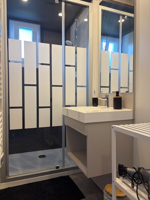 Een moderne badkamer met een douchecabine van glas, een wit wastafelmeubel en een spiegel.
